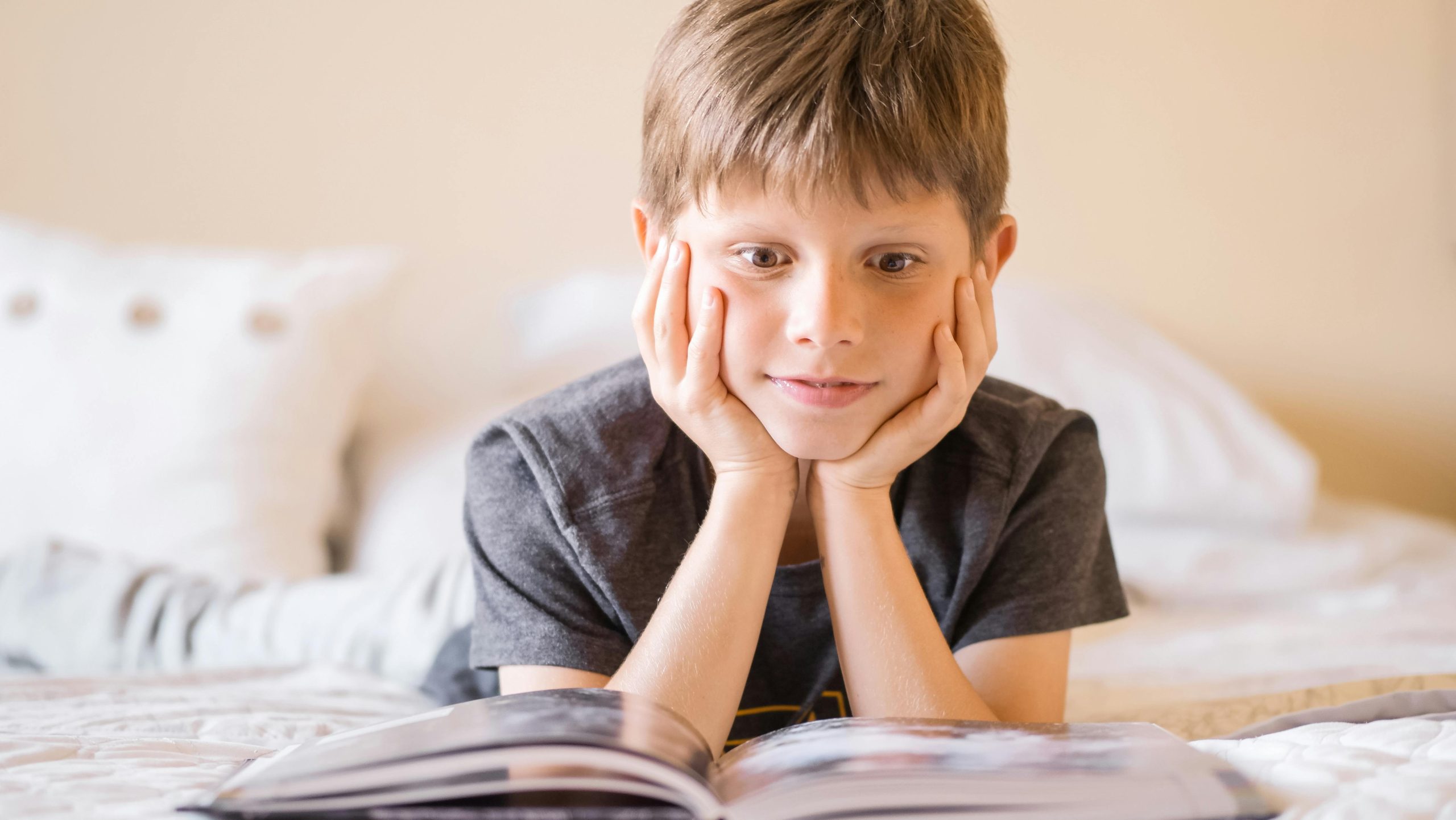Young boy lying on bed, absorbed in a book, illustrating curiosity and learning.